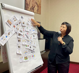 Woman stands next to flip chart with images on it. A man stands next to her. 