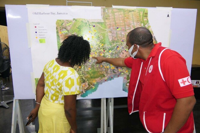 A Red Cross staff member looks at map of Old Harbour Bay with a Resilient Islands stakeholder. The map shows hazards, vulnerabilities and exposed areas in the community.
